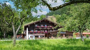 A traditional wooden chalet with a balcony, surrounded by lush greenery and a mountainous backdrop. - Vacation apartment Hirschgwai 50sqm with balcony (Oberaudorf)