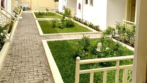 A corridor with a paved walkway, white railings, and small gardens with green grass and red flowers. - Am Place Luxury Apartments (Abuja)