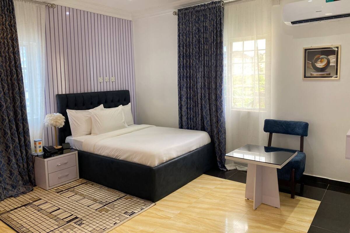 A modern bedroom with a large bed, a small desk, a chair, and a decorative vase.
