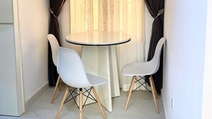 A small, well-lit room with a round table and two white chairs, featuring dark curtains and a light fixture. - Am Place Luxury Apartments (Abuja)