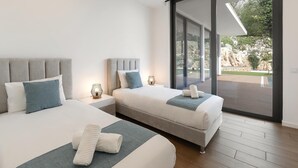 A modern bedroom with two beds, a large sliding glass door leading to an outdoor area, and a view of a rocky landscape. - Luxe & Charme Résidence (Porto de Mos)