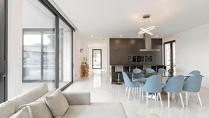 A modern kitchen with dark cabinets, a central island, and a dining area with a glass table and blue chairs. - Luxe & Charme Résidence (Porto de Mos)
