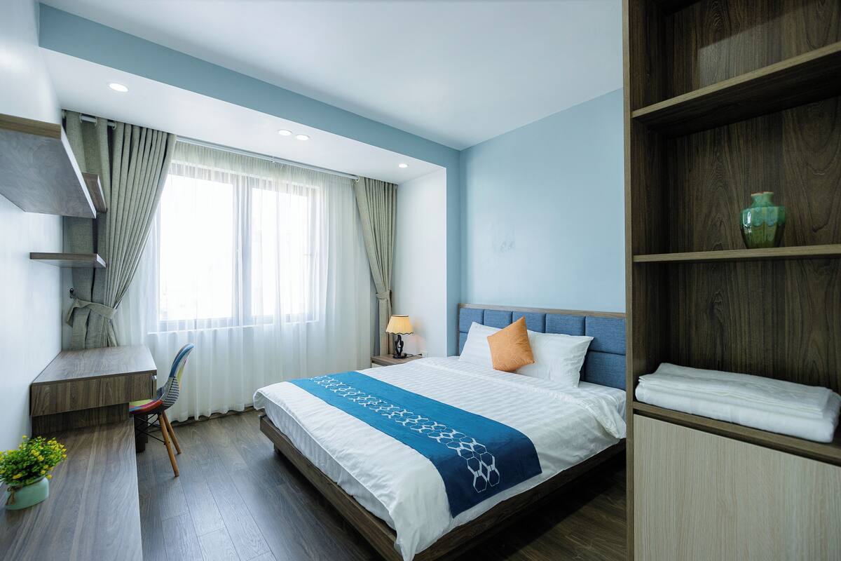 Une chambre d’hôtel avec un lit, un bureau, une chaise, une bibliothèque et une plante en pot.