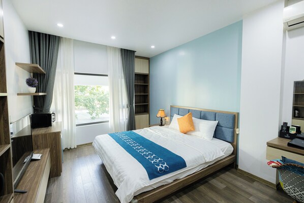 A modern hotel room with a large bed, a desk, a TV, and a window with curtains.
