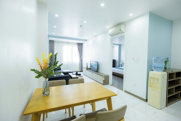 Una habitación de hotel moderna con zona de comedor, sofá, televisor y dispensador de agua.