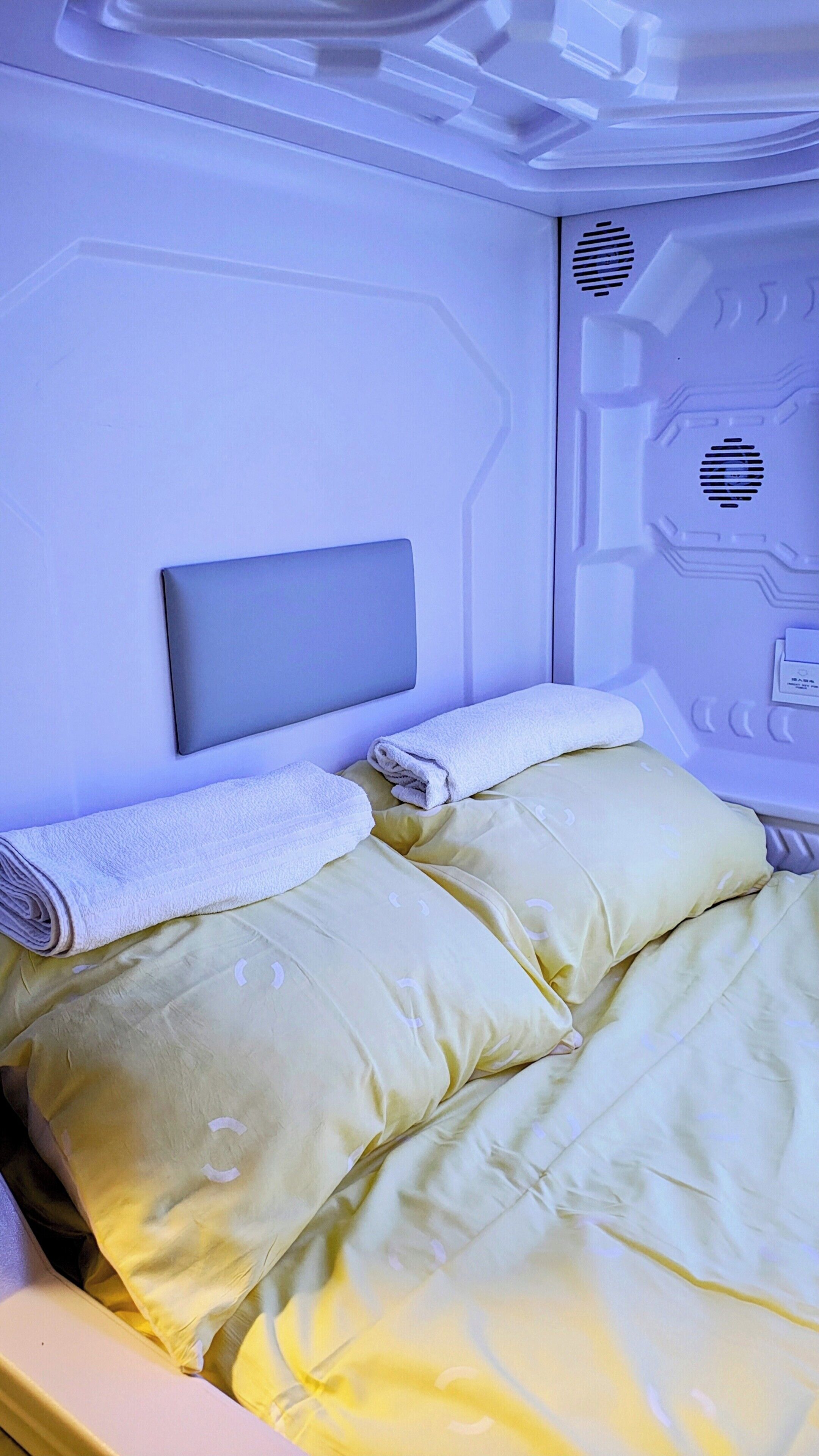 Una cama con cabecera, almohadas y una toalla enrollada.