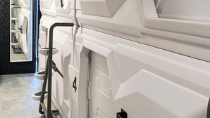 A row of white, modern, wall-mounted toilets with a geometric design, a visible control panel, and a tiled floor. - Capsule hostel Floor -1 Self Check in (Warsaw)