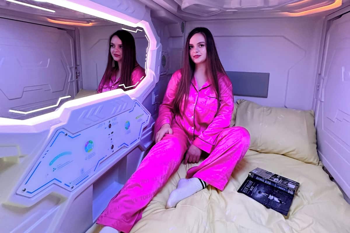 Ein Zimmer im futuristischen Design, mit einem Bett, einem Buch und einer Wand mit einer geometrischen Leuchte.