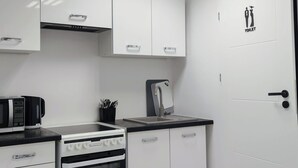 A modern kitchen with white cabinets, a black countertop, a stove, and a sink. - Capsule hostel Floor -1 Self Check in (Warsaw)