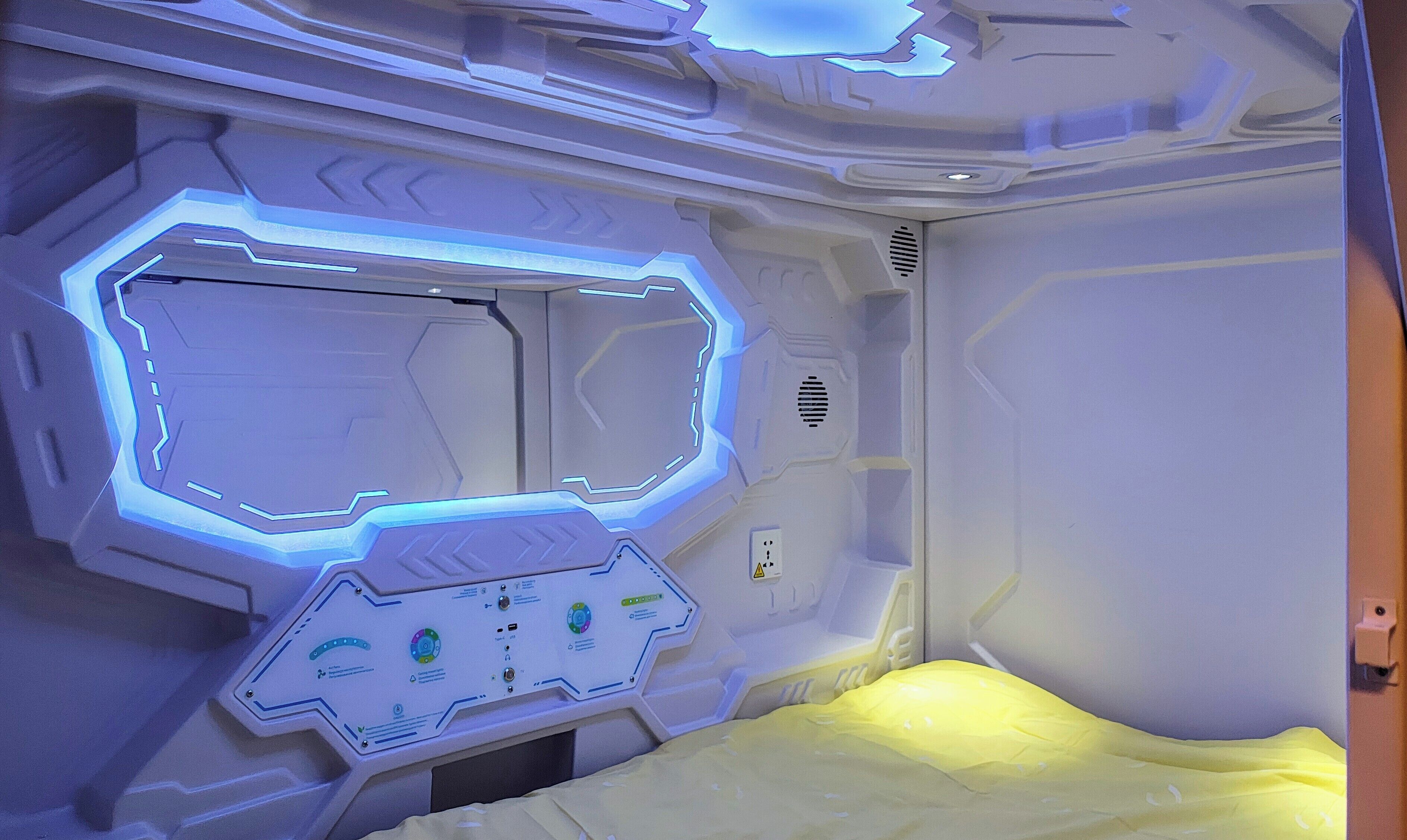 A futuristic room with a central control panel, a bed, and a wall with a geometric pattern.