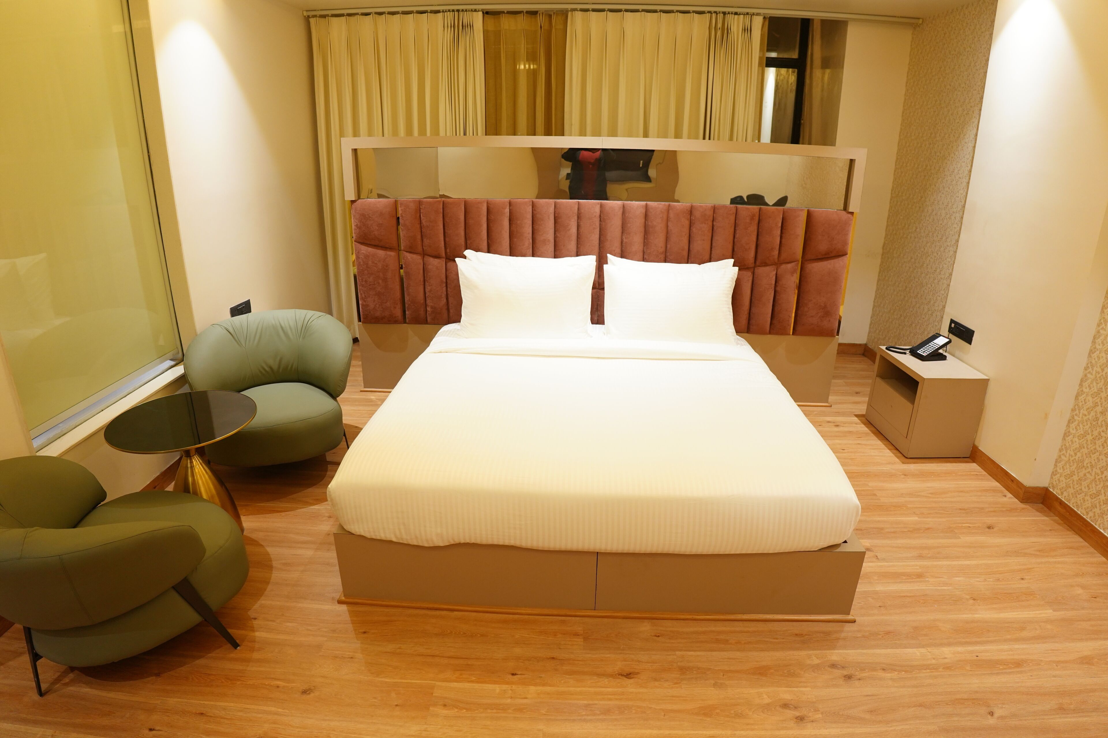 Moderni hotellihuone, jossa on suuri sänky, vihreä nojatuoli, pieni pyöreä pöytä ja sängyn vieressä oleva puhelin.