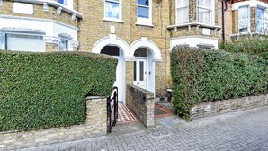 A row of terraced houses with a central entrance, brick walls, and a hedge. - Modern Oasis: 2BR Escape with Outdoor Retreat (London)