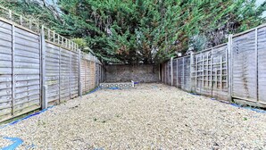 A fenced backyard with a gravel ground, a wooden fence, and a large evergreen tree. - Modern Oasis: 2BR Escape with Outdoor Retreat (London)