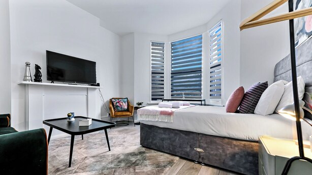 A modern bedroom with a bed, a TV, a small table, and a chair. - Modern Oasis: 2BR Escape with Outdoor Retreat (London)