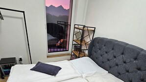 Una camera da letto con un letto, una finestra vista montagne, una libreria e una scrivania con una lampada.