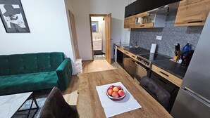 Una cucina compatta con elettrodomestici moderni, un tavolo da pranzo con una ciotola di frutta e un divano verde.