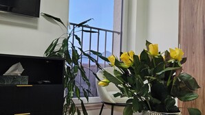 Una camera moderna con un tavolo in marmo, una pianta in vaso con fiori gialli, un mobile TV nero e vista sul cielo attraverso una finestra.
