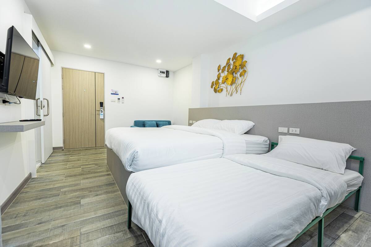 A hotel room with two beds, a TV, a wooden door, and a wall-mounted air conditioning unit.
