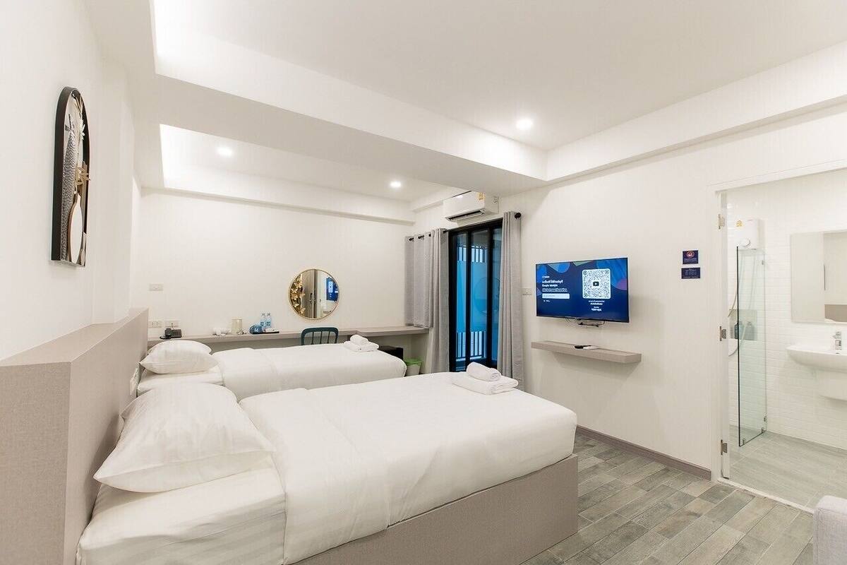 A hotel room with two beds, a TV, a bathroom with a glass shower, and a balcony with a view.