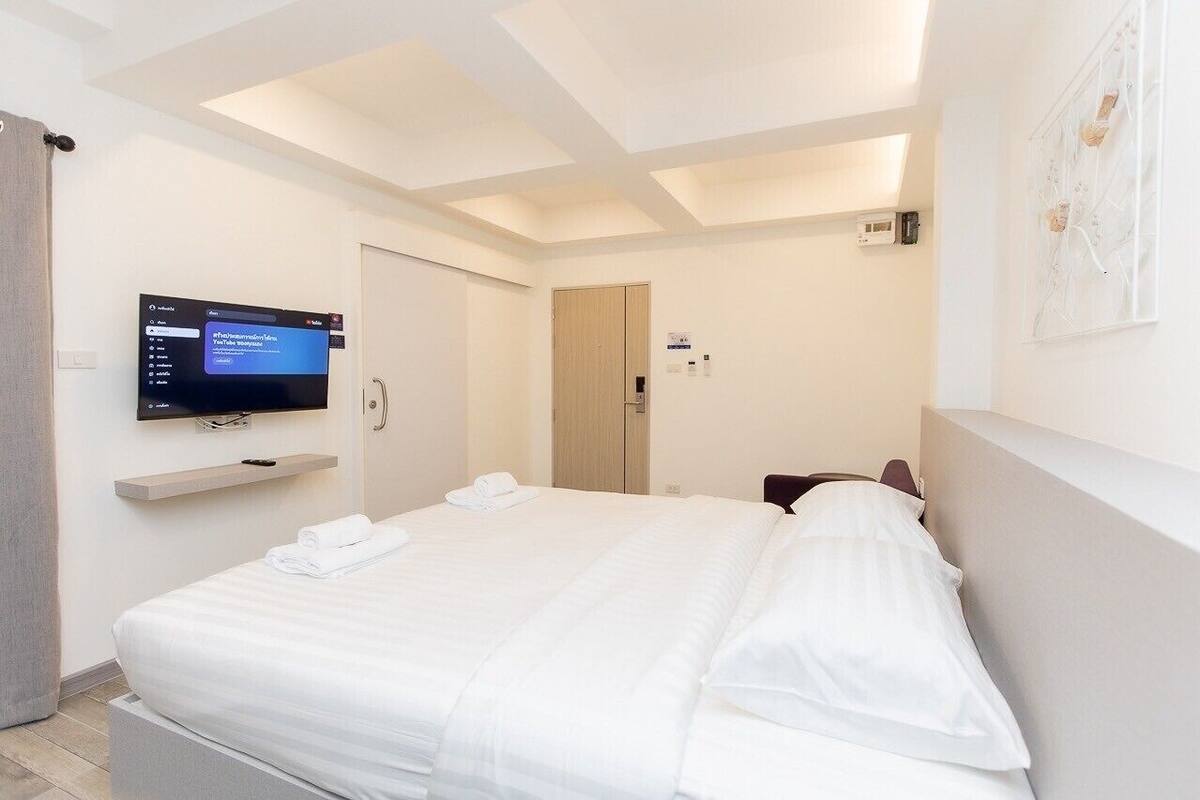 A hotel room with a large bed, a flat-screen TV mounted on the wall, a wooden door, and a light-colored wall.