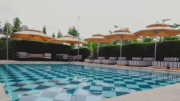 A pool with checkered tiles, lounge chairs, and umbrellas. - ABUS APARTMENT (Asaba)