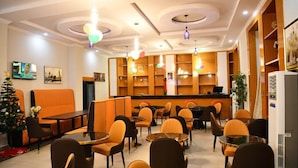 A hotel lobby with orange seating, a reception desk, and a Christmas tree. - ABUS APARTMENT (Asaba)