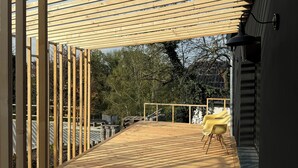 Une terrasse en bois avec une structure en forme de pergola, une chaise jaune et un luminaire noir fixé au mur.