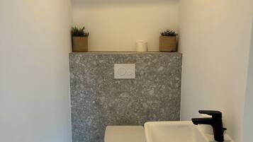A compact bathroom with a toilet, sink, and two potted plants on the wall.