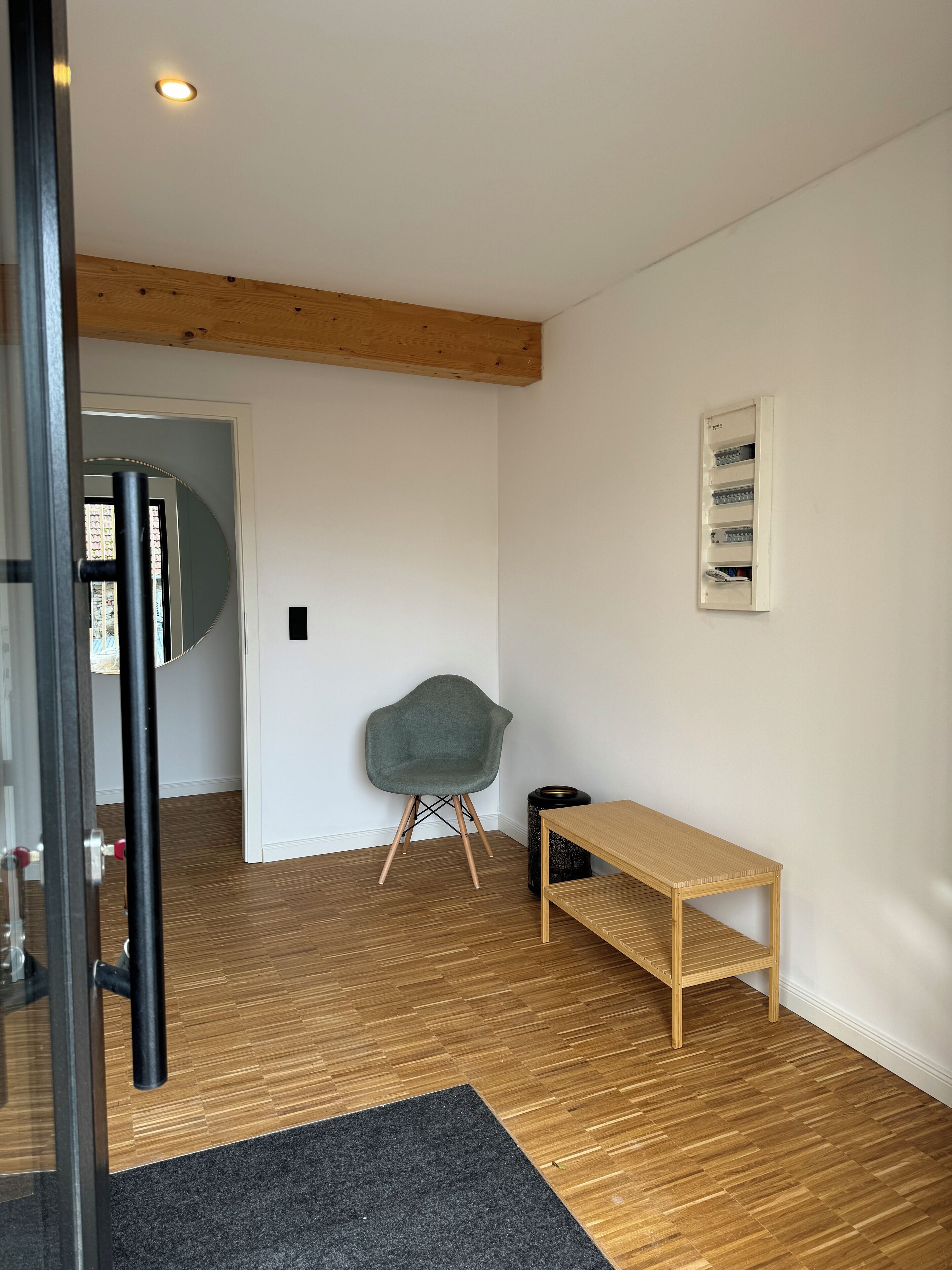 Een modern interieur met een houten vloer, een grijze stoel, een houten bank en een witte muur met een ingelijst beeld.