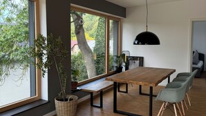 Un espace repas moderne avec une table et des bancs en bois, de grandes fenêtres et un luminaire suspendu.
