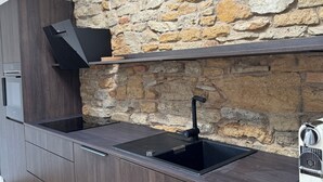 Une cuisine avec des meubles de couleur bois foncé, un mur en pierre et un évier encastré.