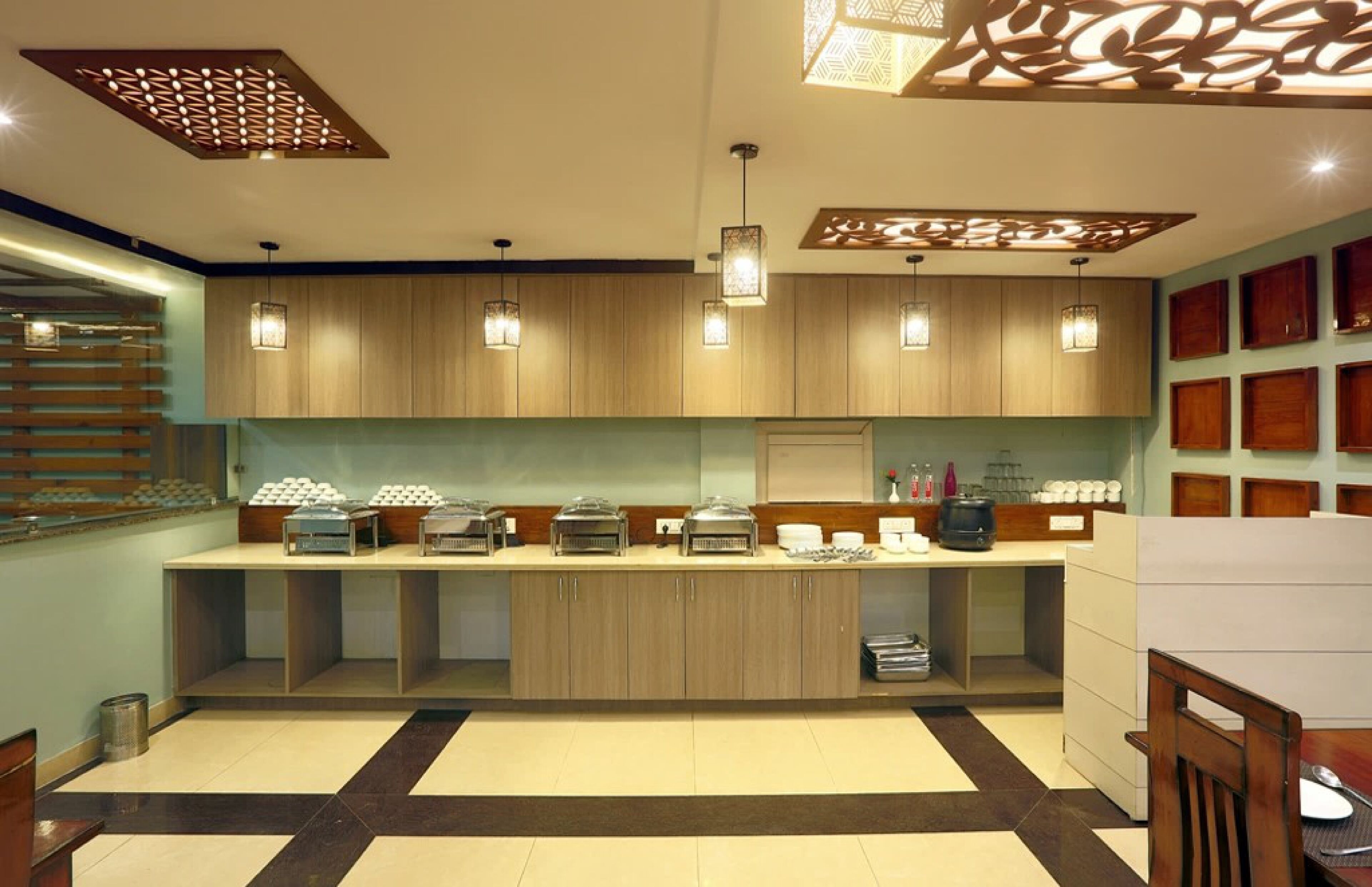 A modern kitchen with wooden cabinets, pendant lights, and a buffet setup.