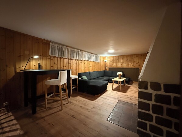A cozy room with a wooden floor, a black sofa, a small table with a vase, and a desk with two chairs.