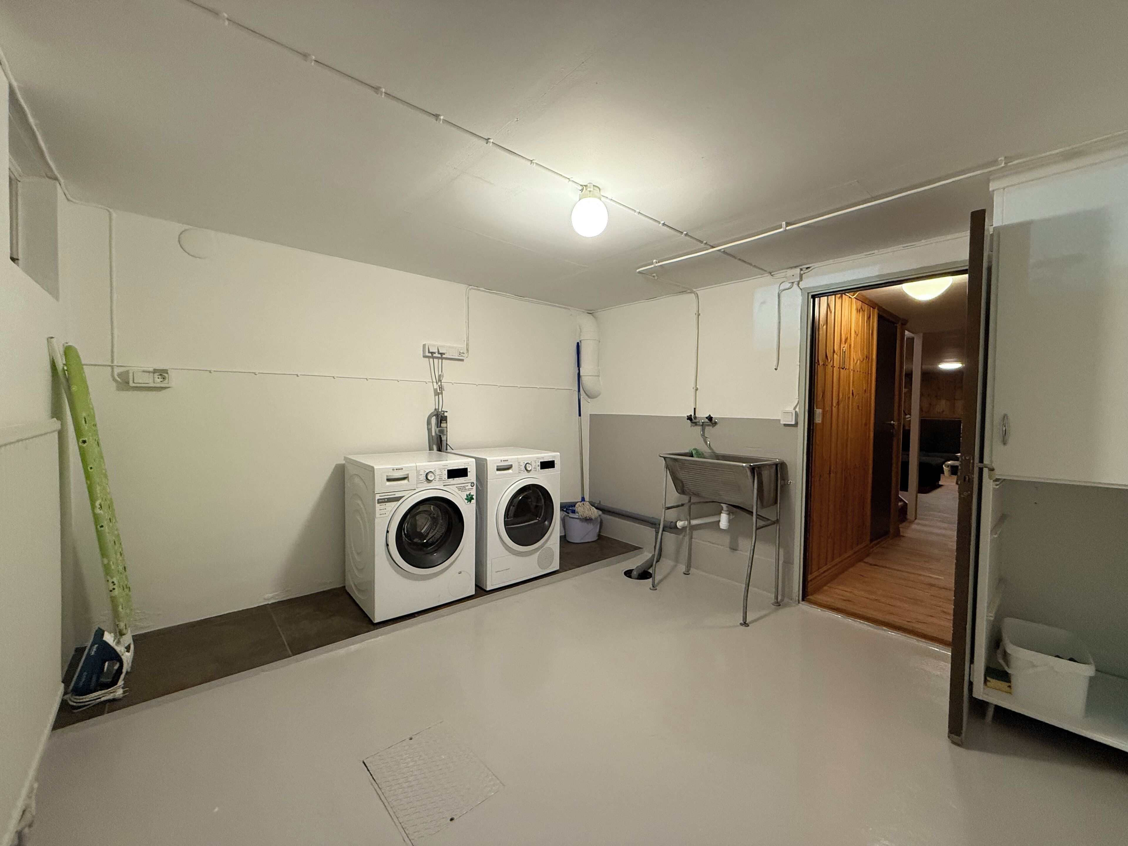 A laundry room with two front-loading washing machines, a small sink, and a drying rack.