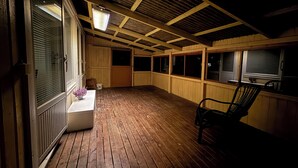 Eine überdachte Holzterrasse mit einer Bank, einem Tisch mit einer Vase und einer Tasche mit dem Aufdruck 'RUSTA'.