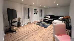 Ein modernes Wohnzimmer mit Flachbildfernseher, einer Couch, einem Couchtisch und einem rosa Sessel.