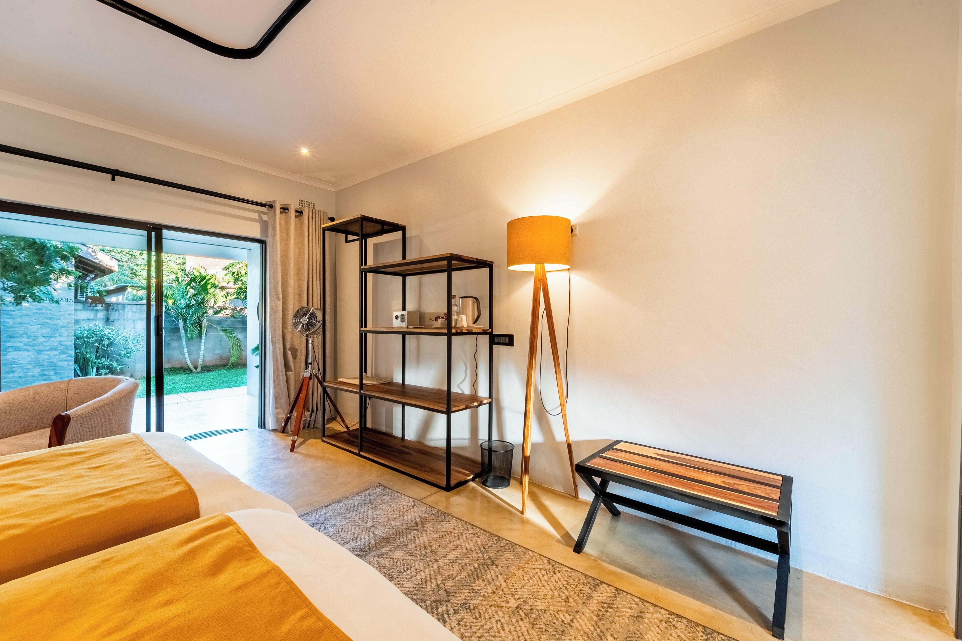 Una habitación de hotel moderna con una cama grande, un banco de madera, una lámpara de pie y un estante negro.