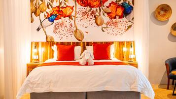 A hotel room with a large bed, red and white bedding, a decorative wall mural, and a wooden nightstand with a lamp.