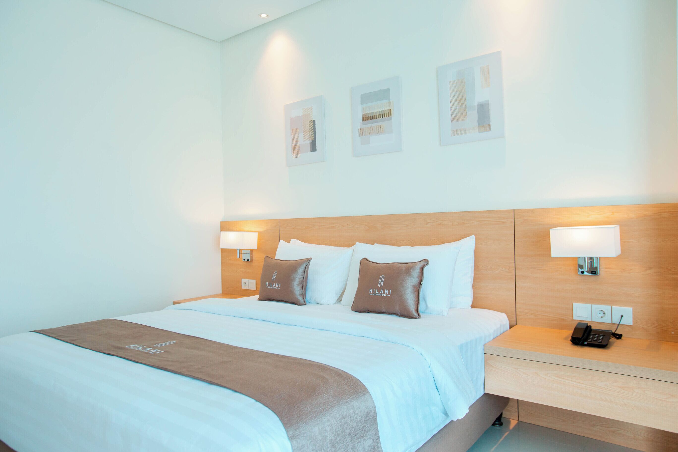 A hotel room with a large bed, two pillows with the brand name, bedside lamps, a bedside phone, and a wall-mounted light.