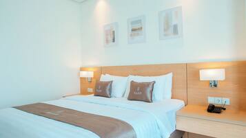 A hotel room with a large bed, two pillows with the brand name, bedside lamps, a bedside phone, and a wall-mounted light.