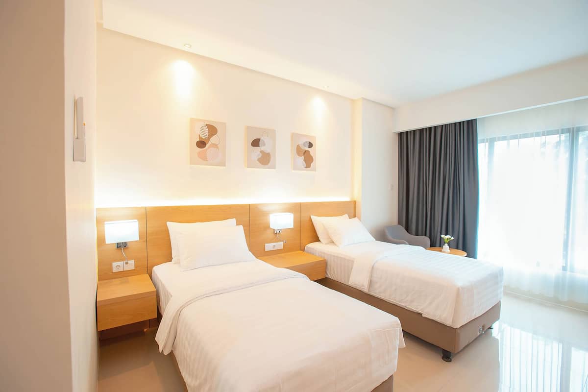 Quarto de hotel com duas camas, cabeceira de madeira, abajures e uma obra de arte na parede.
