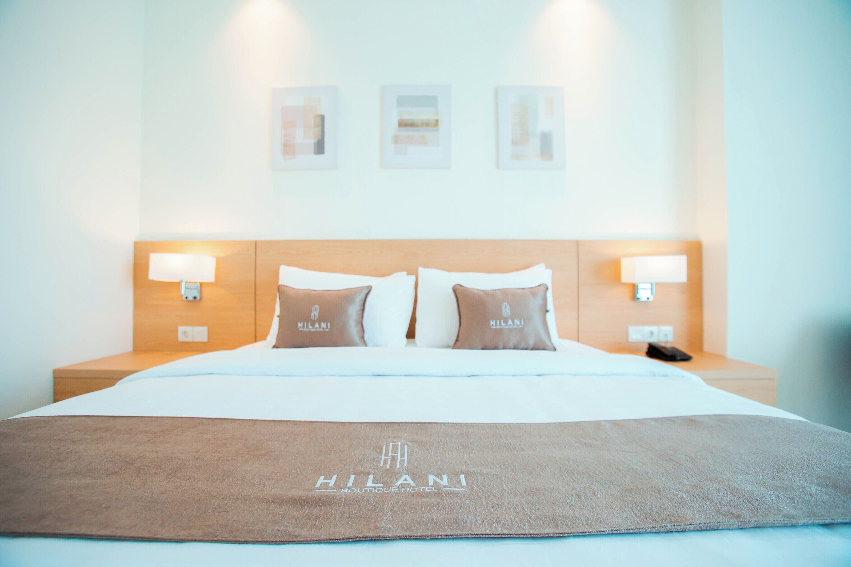 Ein Hotelzimmer mit einem Bett, zwei Kissen mit dem Hotel-Logo, Nachttischlampen und einem Nachttisch mit Telefon.