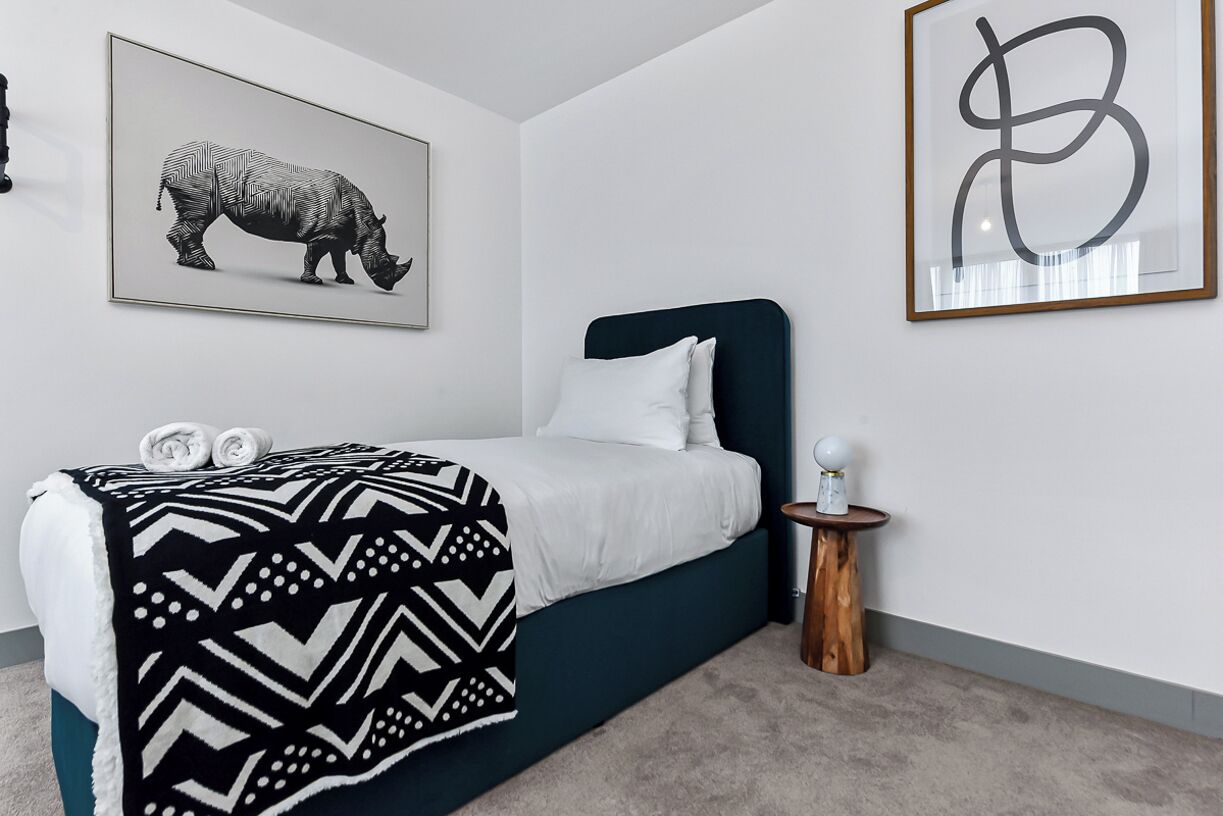 Une chambre à coucher comprenant un lit, une table de chevet, une œuvre d’art représentant un rhinocéros accrochée au mur, et une œuvre d’art abstraite encadrée.