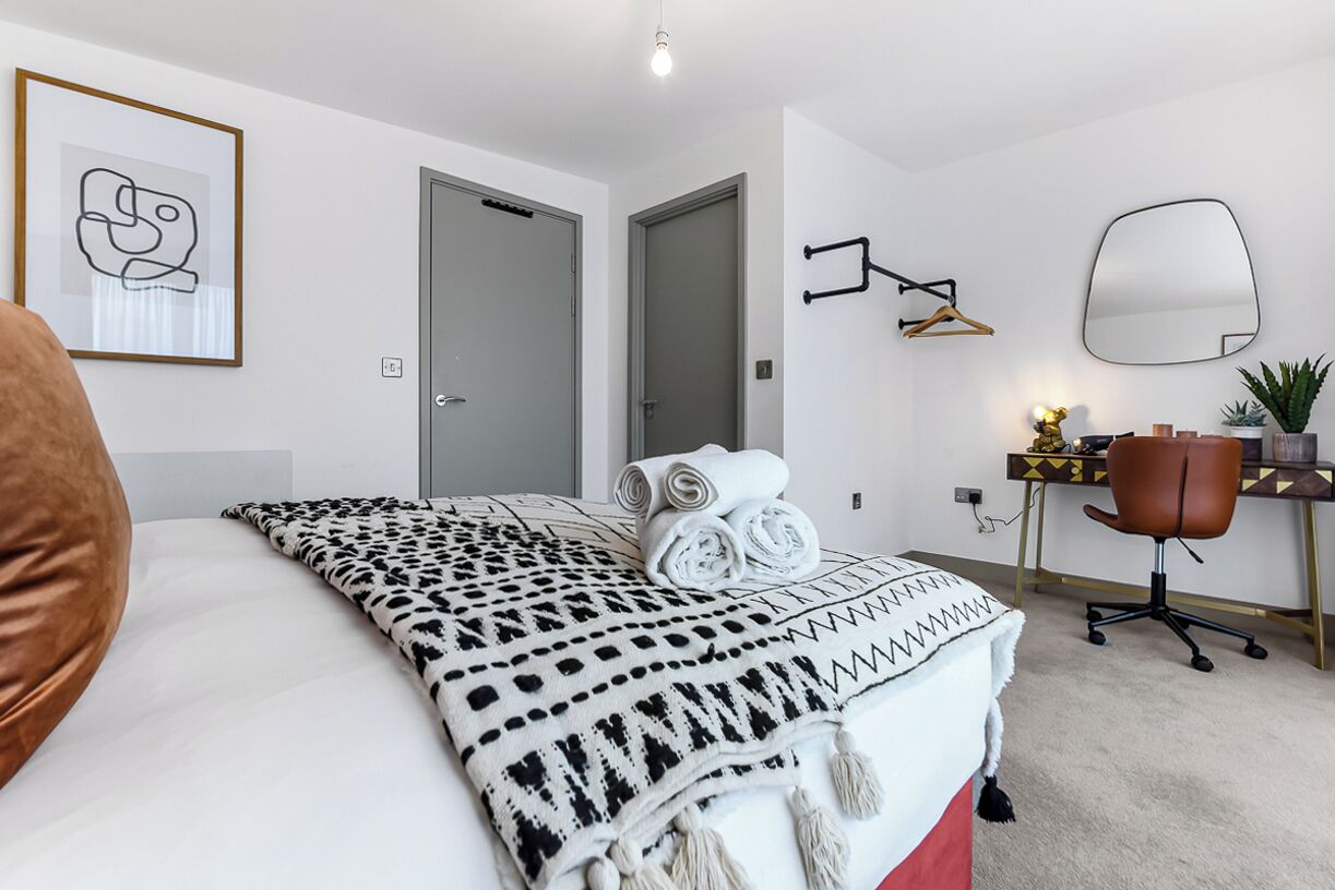 Une chambre moderne avec un grand lit, un bureau et une chaise. On y trouve une porte et un tableau encadré au mur.