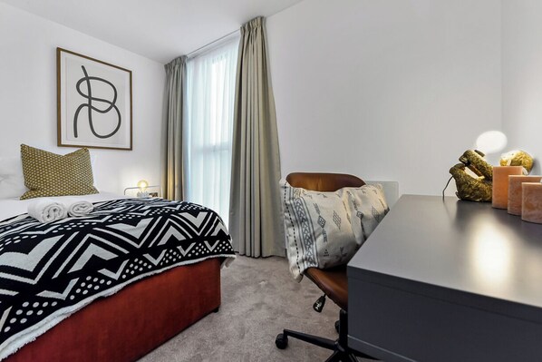 Een hotelkamer met een bed, een bureau, een stoel, een lamp en een raam met gordijnen.