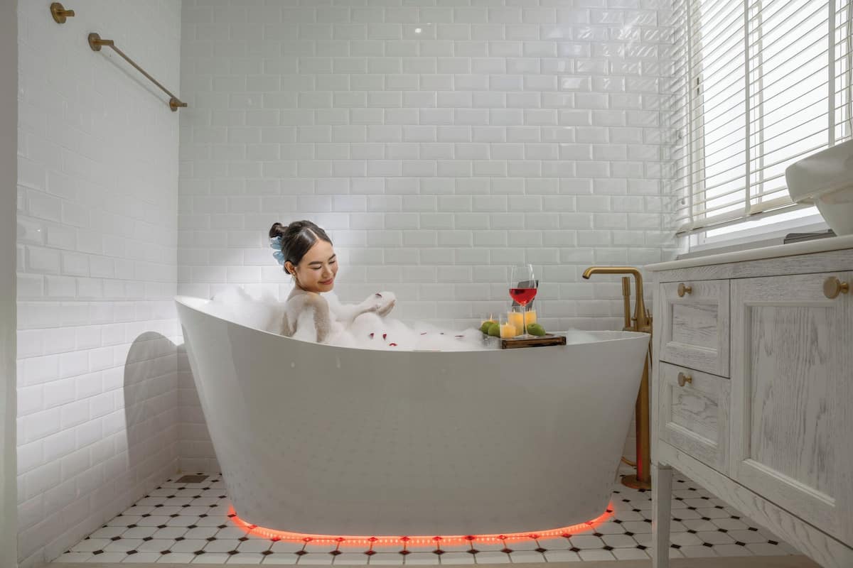 Une baignoire contenant une personne, entourée de bougies et d’un panier de fruits.