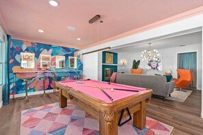 Una mesa de billar en una sala con un mural llamativo, una zona de bar y un sofá moderno.