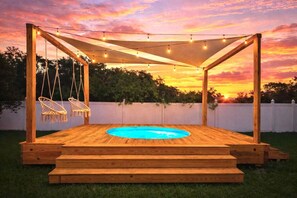 Terraza de madera con piscina, sillas colgantes y luces de cuerda.