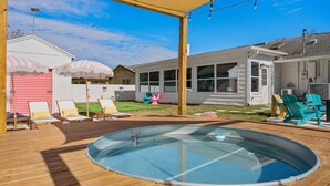 Un patio trasero con jacuzzi, terraza de madera y mobiliario exterior.