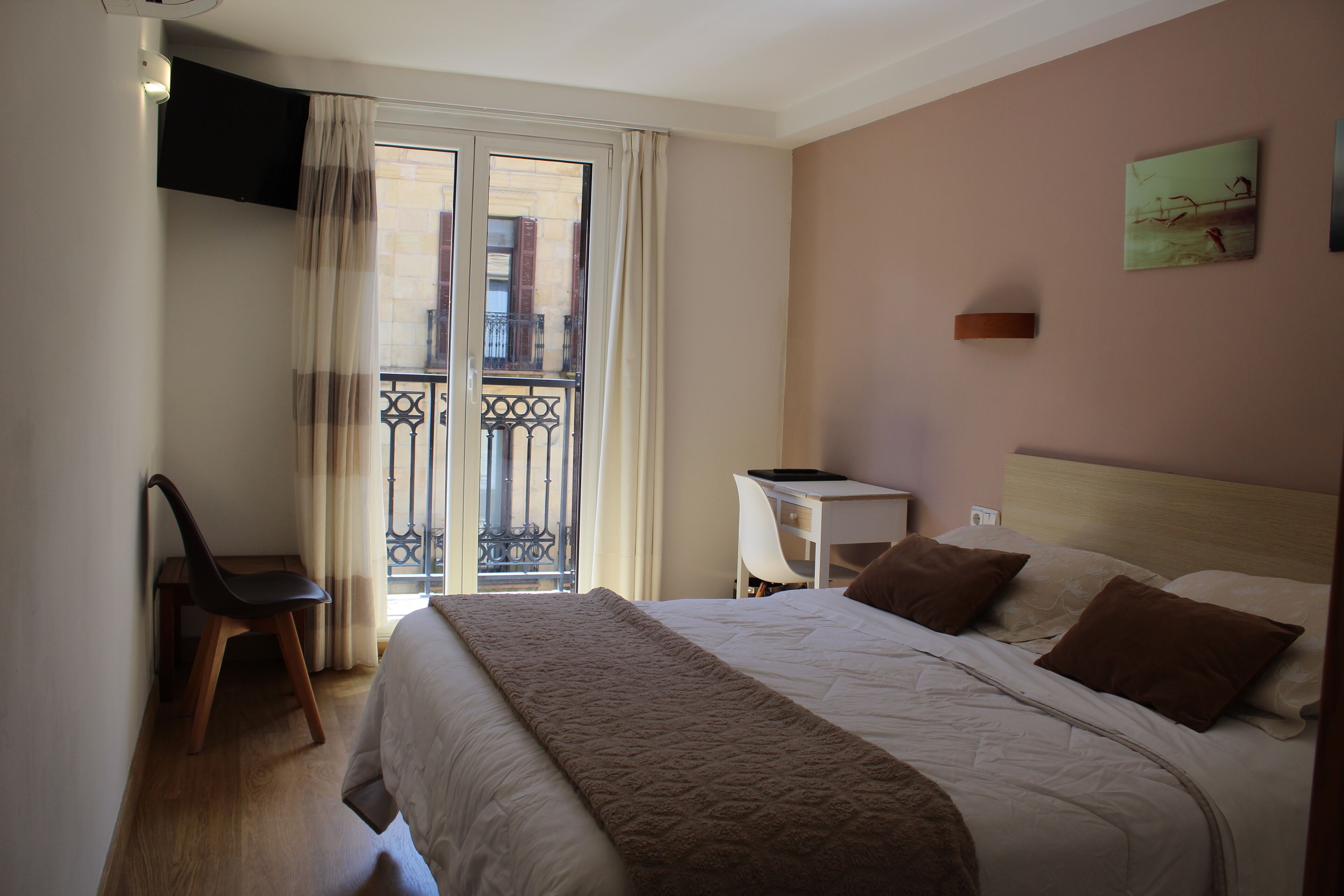 A hotel room with a bed, a desk, a chair, and a view of the outside balcony.